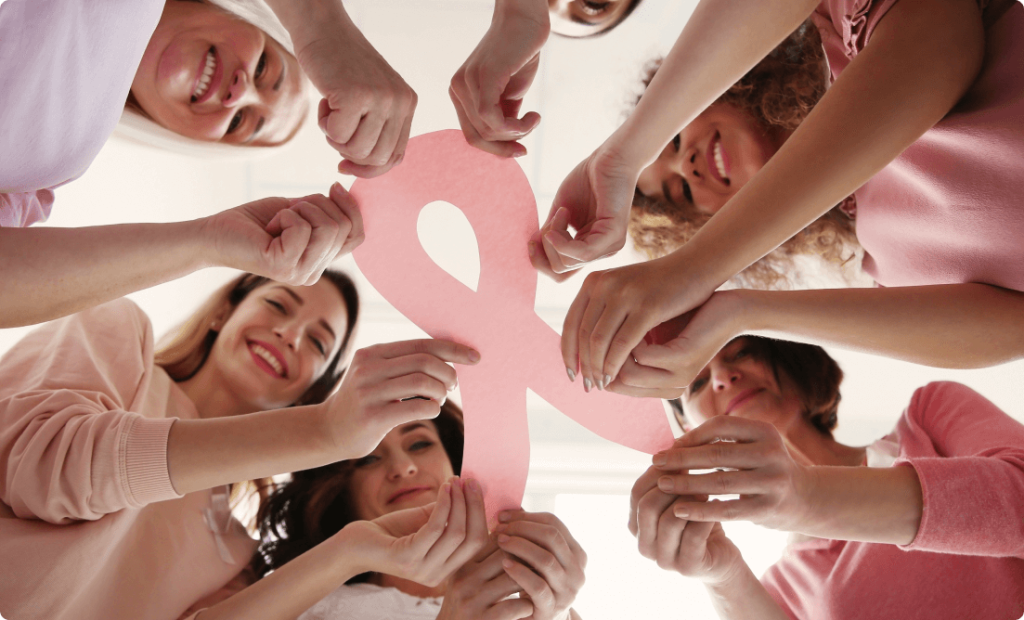 A group of Women wearing pink and holding a pink ribbon to show support for the people affected by breast cancer.