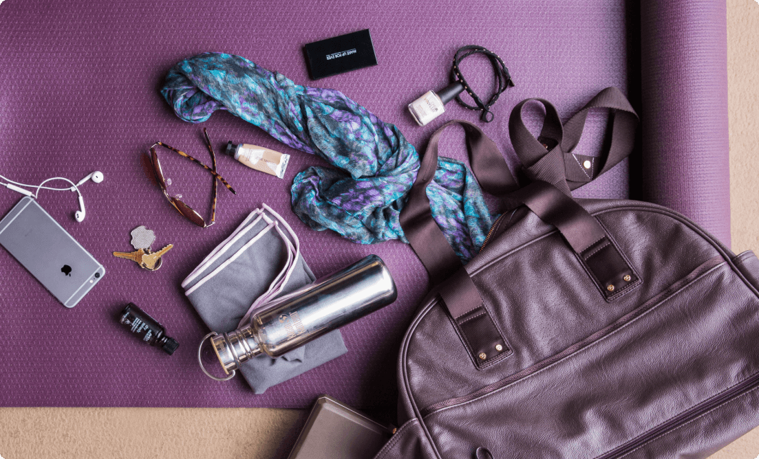  A purple gym bag placed on a purple yoga matt containing a water bottle, sweat towel, iphone, earphones, sunglasses and some cosmetics.