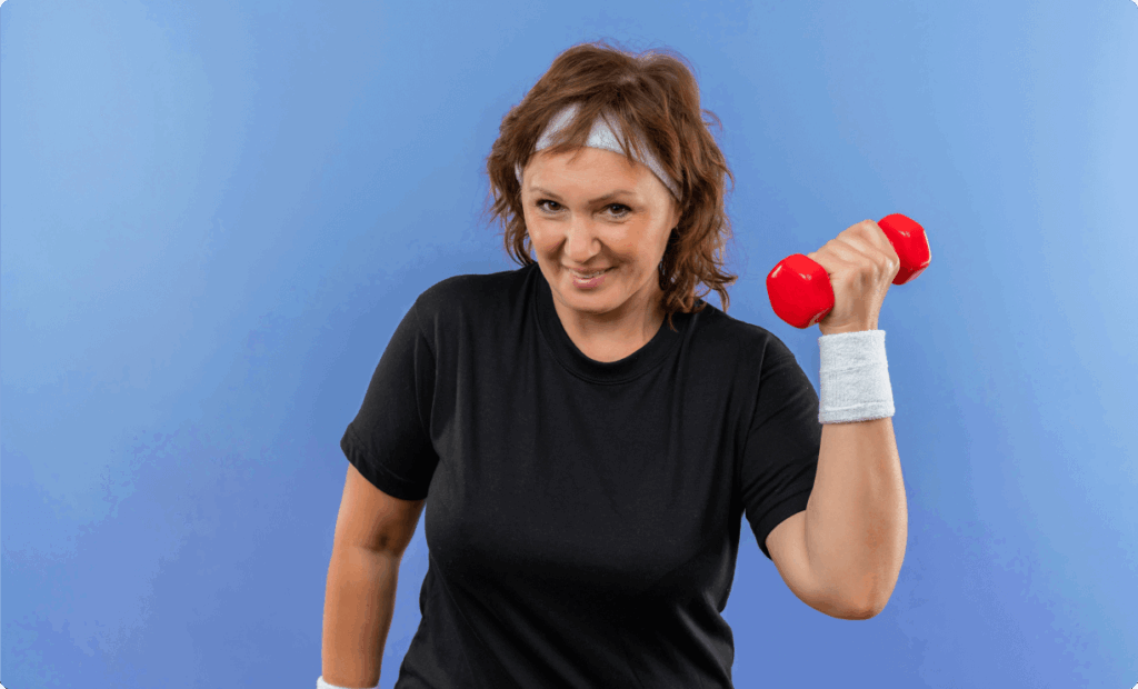 Smiling middle-aged woman in workout clothes lifting a red dumbbell against a blue background, promoting strength training and fitness at Vision Elite Training