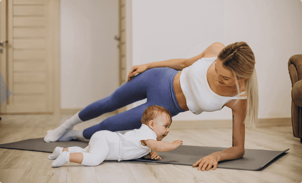 Mother doing a side plank exercise on a yoga mat while smiling at her baby, promoting postpartum fitness and bonding at Vision Elite Training.