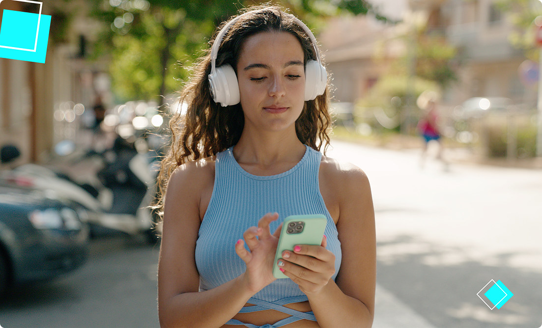 Young woman wearing headphones and selecting a workout playlist on her phone, promoting active summer routines and fitness motivation with Vision Elite Training.