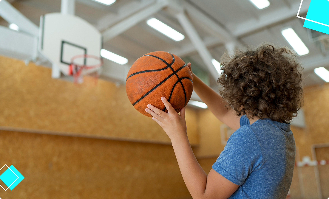 Young student aiming to shoot a basketball indoors, highlighting youth sports and athletic development supported by Vision Elite Training during summer break.